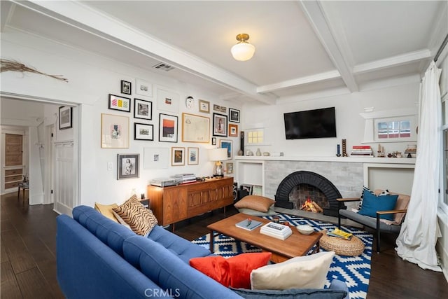 living room featuring beam ceiling, wood finished floors, visible vents, and a warm lit fireplace