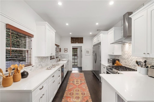 kitchen with stainless steel appliances, wall chimney exhaust hood, dark wood finished floors, and light countertops