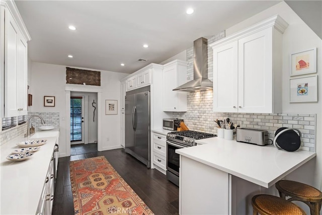 kitchen featuring wall chimney range hood, light countertops, white cabinets, stainless steel appliances, and a sink