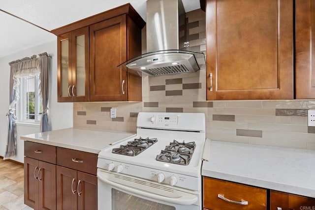 kitchen featuring white gas stove, glass insert cabinets, tasteful backsplash, and wall chimney exhaust hood