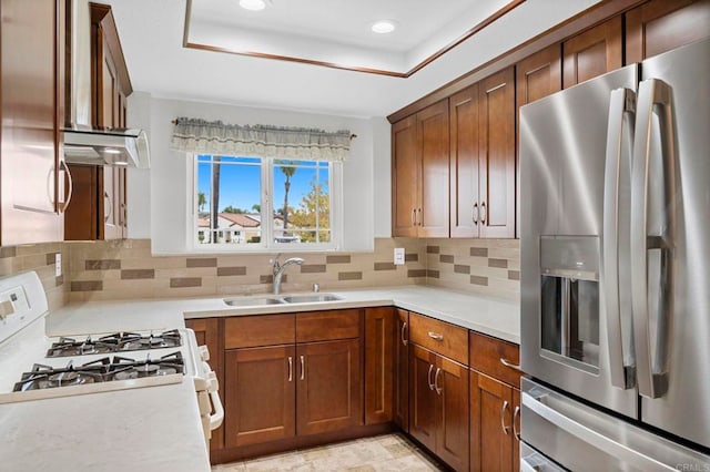 kitchen with stainless steel fridge with ice dispenser, light countertops, white range with gas stovetop, a tray ceiling, and a sink