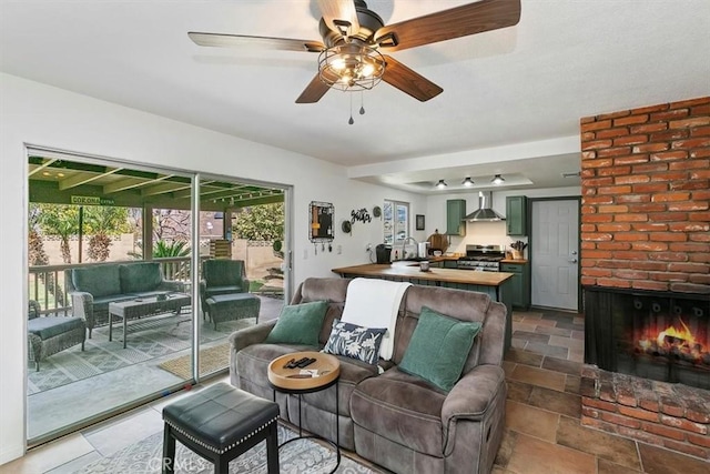 living area with stone finish floor, a brick fireplace, and a ceiling fan