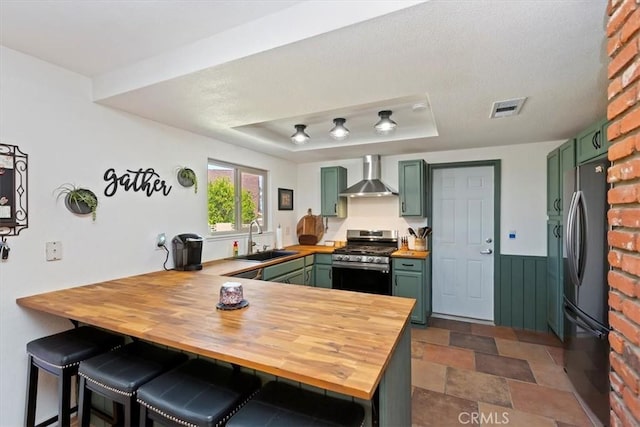 kitchen with a sink, wall chimney exhaust hood, gas range, and green cabinets