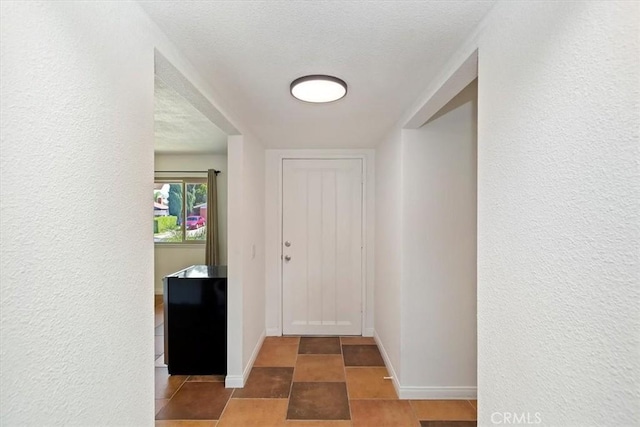 hallway featuring a textured wall, baseboards, and a textured ceiling