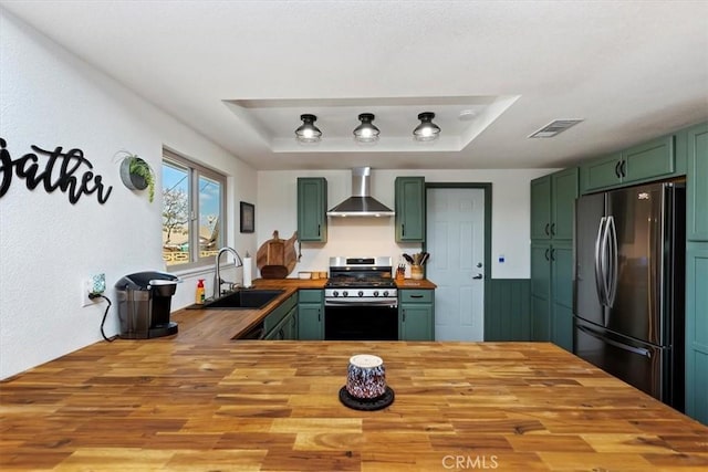 kitchen featuring green cabinetry, freestanding refrigerator, butcher block countertops, gas range, and wall chimney exhaust hood