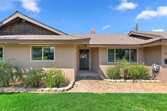 ranch-style house featuring a chimney, stucco siding, a front yard, and roof with shingles