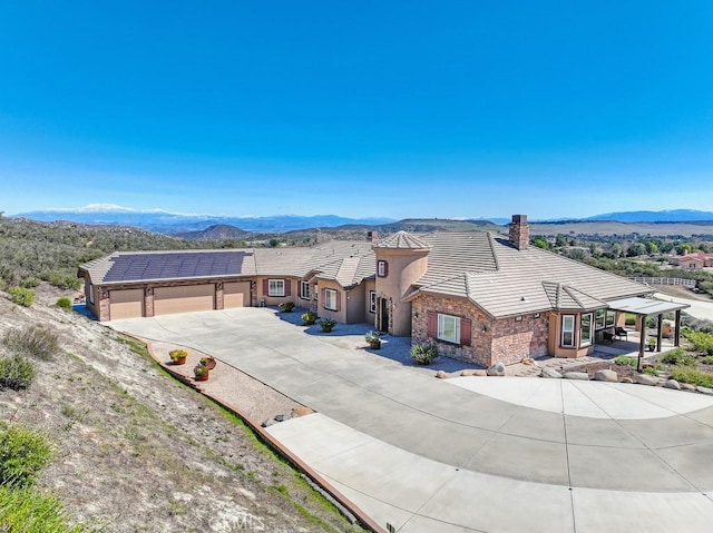 view of front of house featuring an attached garage, a tile roof, concrete driveway, stone siding, and a mountain view