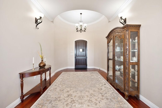 entryway with baseboards, arched walkways, ornamental molding, dark wood-type flooring, and a chandelier