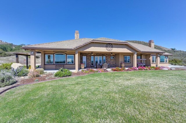 rear view of property featuring a lawn, a chimney, ceiling fan, and stucco siding