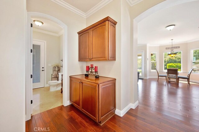 hall featuring dark wood finished floors, crown molding, baseboards, and arched walkways