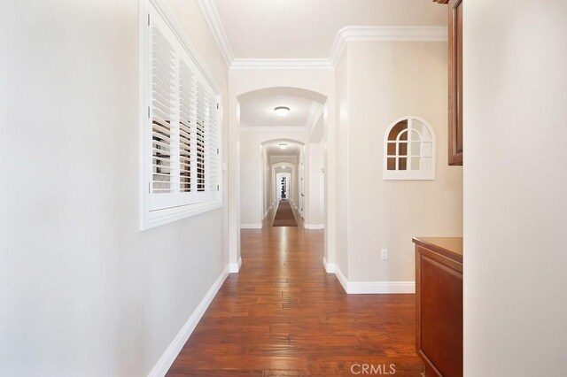 hall with arched walkways, crown molding, dark wood-type flooring, and baseboards