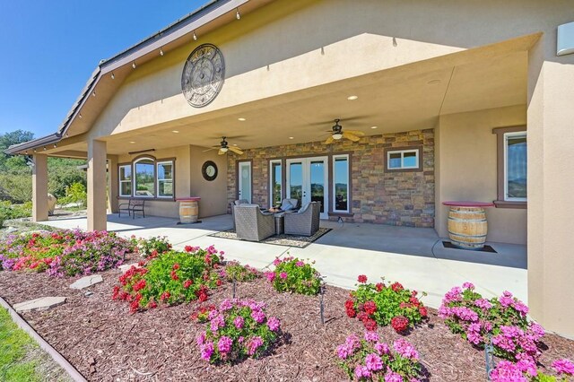 back of property with a patio area, stone siding, stucco siding, and ceiling fan