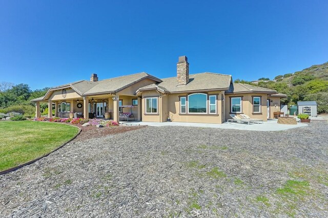 rear view of house with a tiled roof, stucco siding, a chimney, a yard, and a patio area