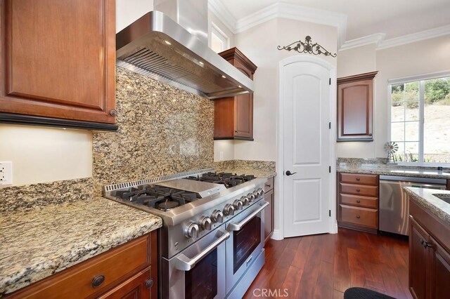 kitchen with crown molding, light stone counters, stainless steel appliances, wall chimney exhaust hood, and dark wood-style flooring