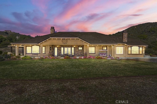 view of front of house featuring stucco siding, a lawn, a chimney, and a tiled roof