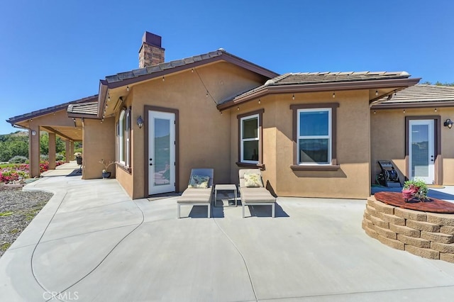 rear view of property with a patio area, a chimney, and stucco siding