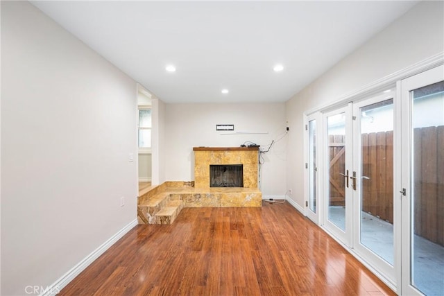 unfurnished living room with recessed lighting, a fireplace with raised hearth, baseboards, and wood finished floors