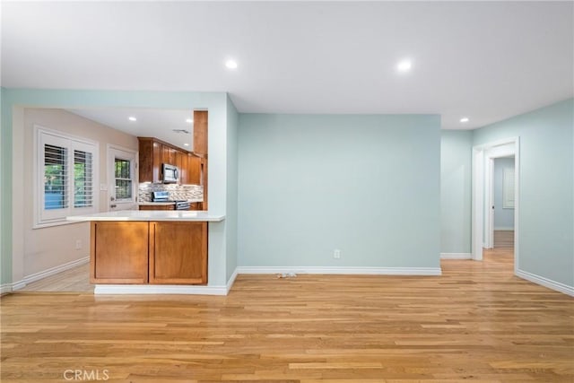 kitchen with backsplash, baseboards, light wood-type flooring, and appliances with stainless steel finishes