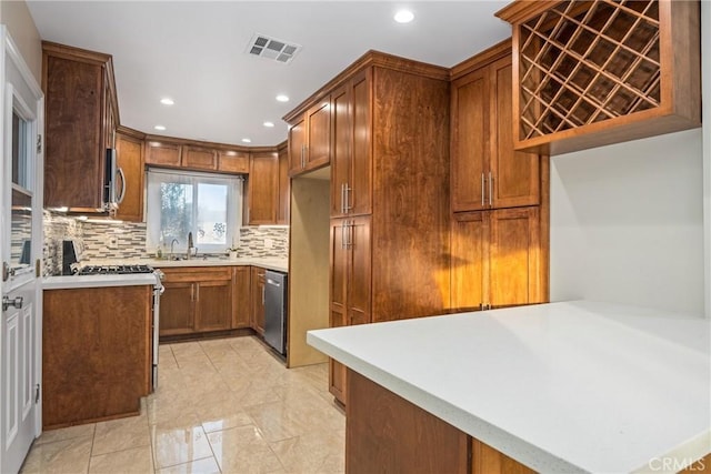 kitchen with visible vents, stainless steel appliances, a sink, brown cabinets, and backsplash