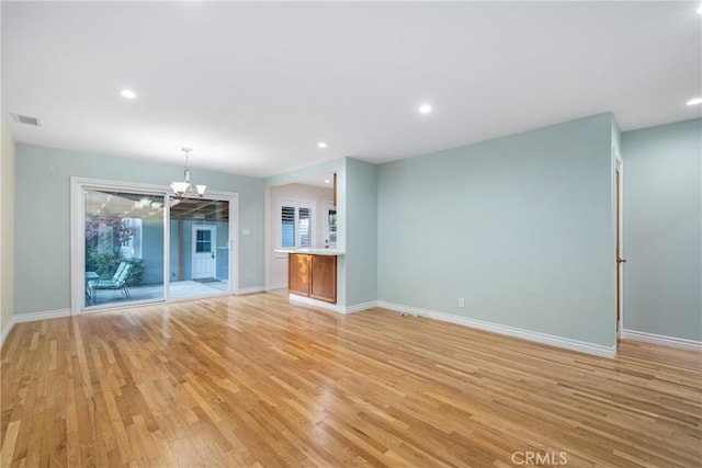 unfurnished living room featuring a chandelier, visible vents, baseboards, and light wood-style floors