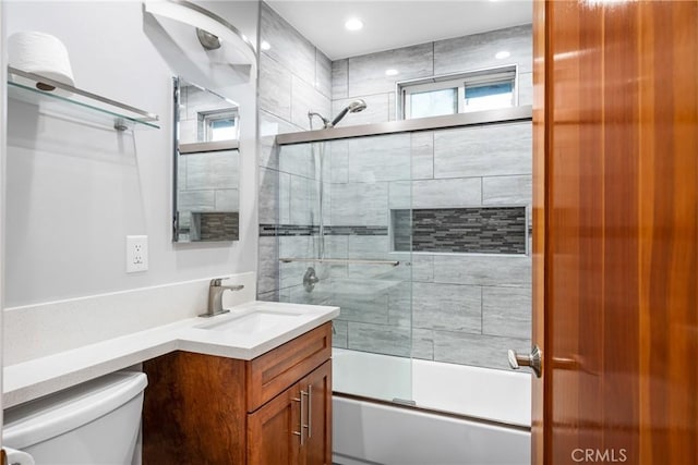 bathroom with combined bath / shower with glass door, a healthy amount of sunlight, toilet, and vanity