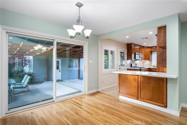 kitchen with light wood finished floors, a peninsula, appliances with stainless steel finishes, a notable chandelier, and backsplash