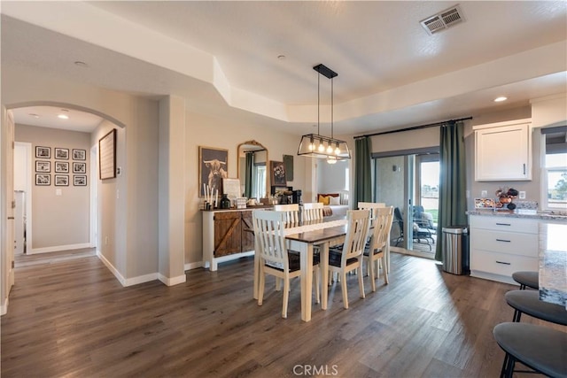 dining space featuring dark wood-style floors, visible vents, baseboards, arched walkways, and a raised ceiling