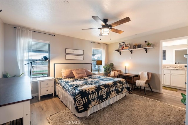 bedroom with ceiling fan, baseboards, light wood-style flooring, and ensuite bathroom