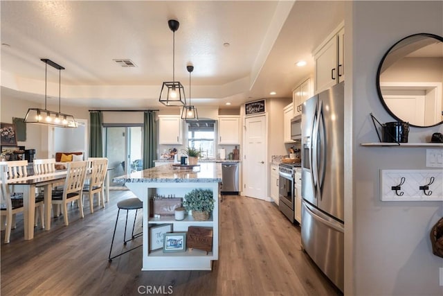 kitchen with light stone counters, white cabinetry, stainless steel appliances, and a raised ceiling