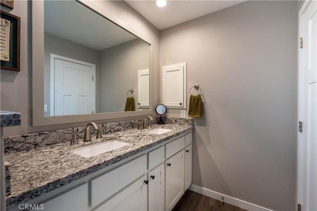 bathroom featuring double vanity, wood finished floors, baseboards, and a sink