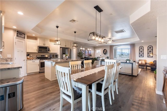 dining area featuring dark wood finished floors, visible vents, and a tray ceiling