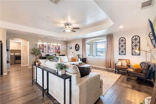 living room featuring a raised ceiling, wood finished floors, visible vents, and washer and clothes dryer