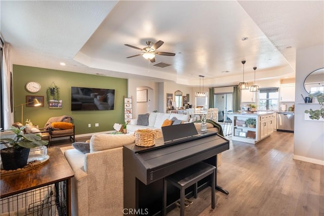 living area with a raised ceiling, light wood-style floors, visible vents, and baseboards