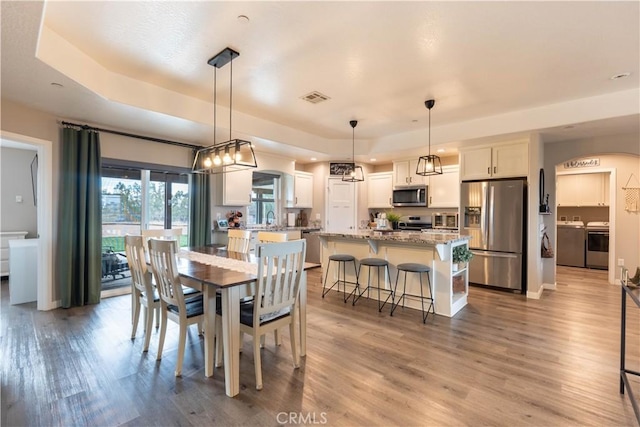 dining area with light wood-style flooring, washing machine and dryer, visible vents, and baseboards