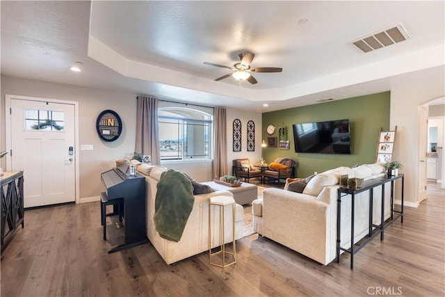 living room featuring visible vents, ceiling fan, baseboards, a tray ceiling, and wood finished floors