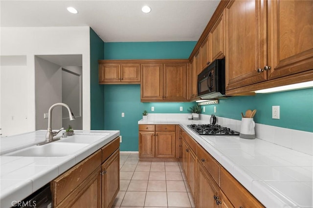 kitchen featuring tile countertops, brown cabinets, black microwave, and a sink