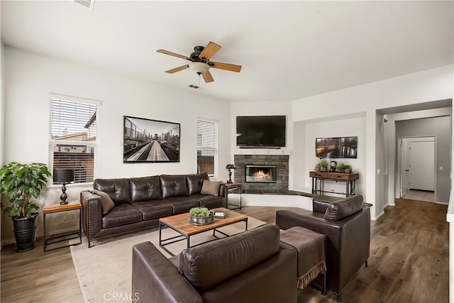 living area featuring visible vents, wood finished floors, a stone fireplace, baseboards, and ceiling fan