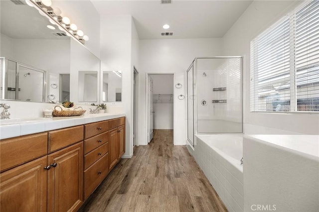 full bathroom with a walk in closet, a stall shower, wood finished floors, double vanity, and a bath