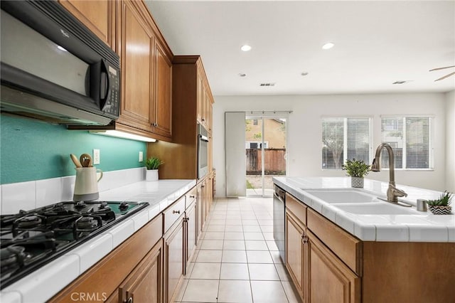 kitchen with tile countertops, brown cabinets, black appliances, and a sink