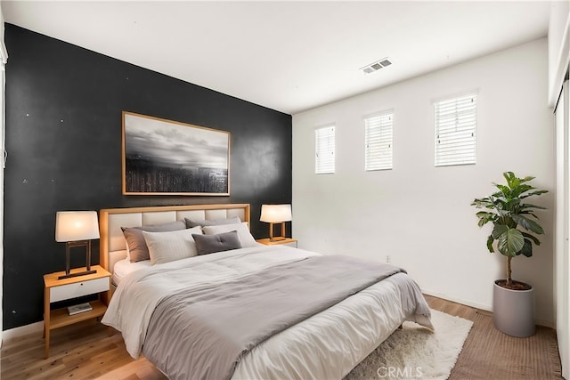 bedroom featuring visible vents, an accent wall, baseboards, and wood finished floors