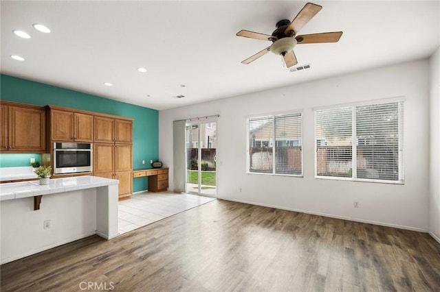 kitchen with tile countertops, visible vents, light wood-style floors, stainless steel oven, and brown cabinets