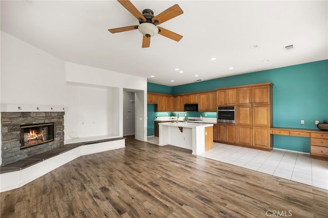 kitchen featuring a ceiling fan, visible vents, oven, black microwave, and open floor plan