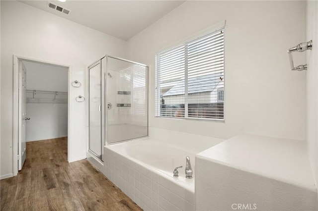 full bathroom featuring visible vents, a walk in closet, a garden tub, a stall shower, and wood finished floors