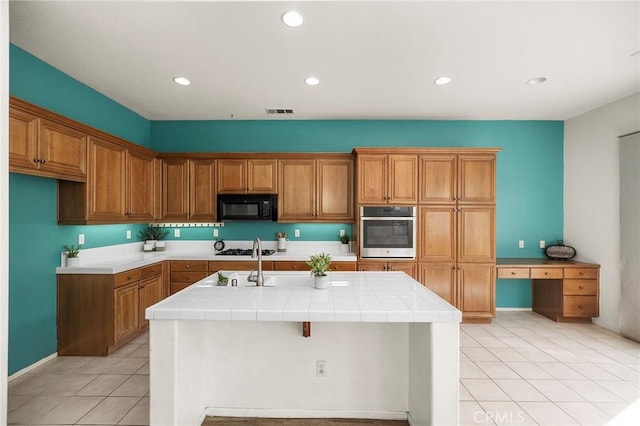 kitchen with visible vents, brown cabinets, black appliances, and tile counters