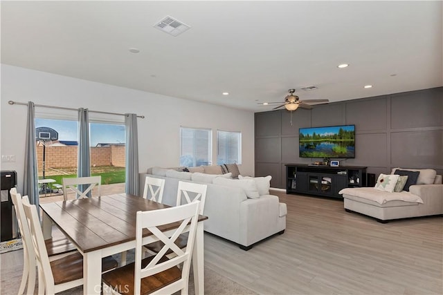 dining room with a decorative wall, visible vents, light wood finished floors, and ceiling fan