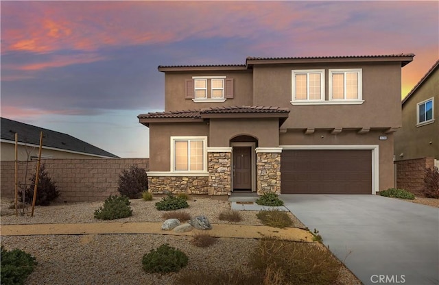 mediterranean / spanish house featuring stucco siding, driveway, stone siding, fence, and a garage