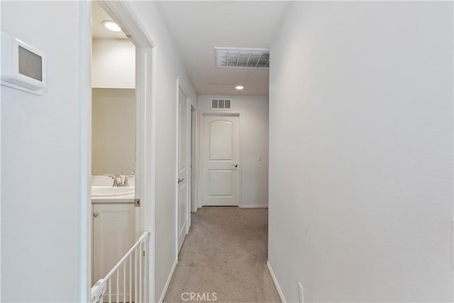 hallway featuring light carpet, visible vents, baseboards, and a sink