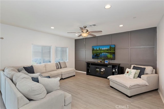 living area with light wood finished floors, a decorative wall, ceiling fan, and visible vents