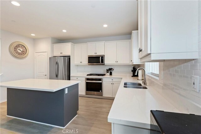 kitchen featuring light wood-style flooring, a sink, appliances with stainless steel finishes, white cabinetry, and backsplash