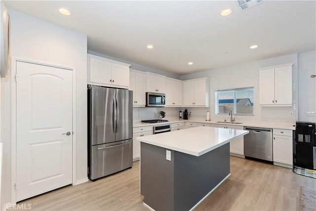 kitchen featuring visible vents, a sink, stainless steel appliances, light wood-style floors, and white cabinetry